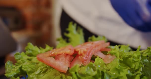 A colocação de mãos de cozinheiro põe tomates e pepinos em um hambúrguer. Fecha. Movimento lento — Vídeo de Stock