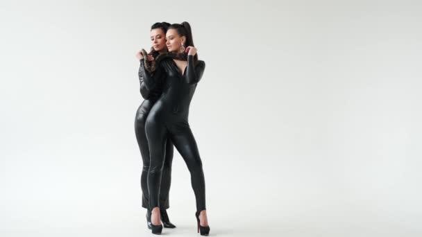 Дві сексуальні жінки в чорному латексі стоять у білій студії зі змією на шиї.. — стокове відео