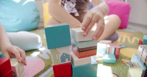 Close up Niños preescolares que ayudan a construir bloques de madera juntos se sientan en la alfombra del piso. — Vídeos de Stock