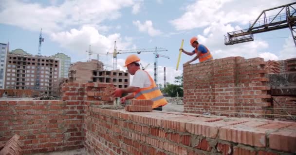 Mužský dělník pokládá cihlu do zdi s cementem pomocí lopaty. — Stock video