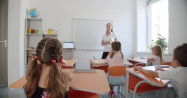 Öğrenciler sınıfta sıralarında oturuyorlar ve cevap vermek için ellerini kaldırıyorlar. Arka plan.