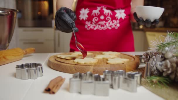 Vista de una mano de mujer haciendo una galleta de jengibre usando una cuchara, pone la mermelada en las galletas. Concepto de Navidad y Año Nuevo — Vídeo de stock