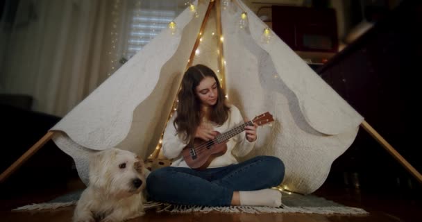 소녀는 강아지 잭 러셀과 함께 유아용 텐트에 앉아 기타를 연주 한다. 강제 2 — 비디오