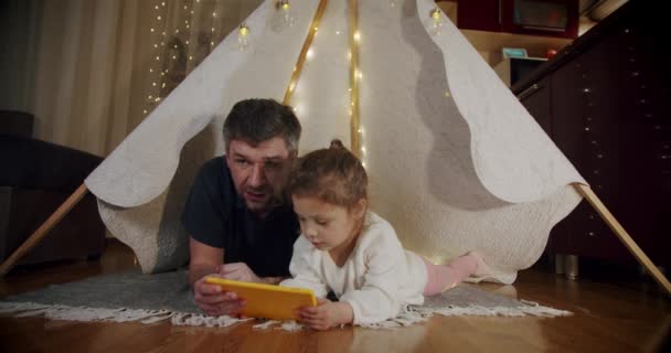 爸爸和女儿晚上在帐篷里玩耍，在平板电脑上看卡通片. — 图库视频影像