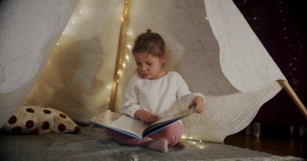 Child in a wigwam tent play at night and read a book. happy family kid dream concept. — Stock Video