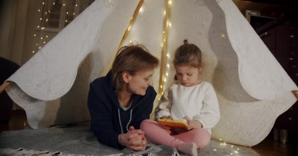 Kızıyla birlikte çadırda gülümseyen, konuşan, tablet kullanan mutlu bir kadın. Vercion 3 — Stok video