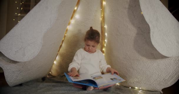 Dziecko w namiocie wigwam bawić się w nocy i czytać książkę. Pomysł szczęśliwego dziecka rodzinnego. Wercyon 2 — Wideo stockowe