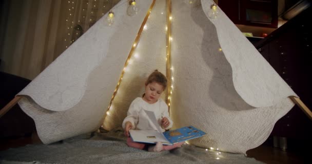 Dziecko w namiocie wigwam bawić się w nocy i czytać książkę. Pomysł szczęśliwego dziecka rodzinnego. Wercyon 3 — Wideo stockowe