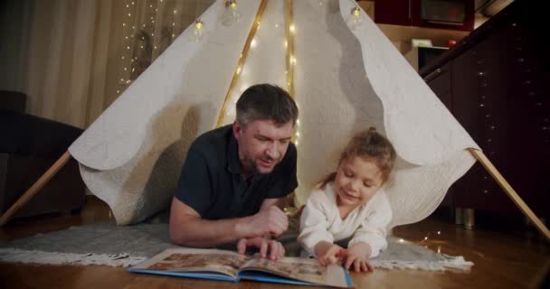 Papà e figlia la sera giocano e guardano cartoni animati su una tavoletta, in una tenda. Vercion 4 — Video Stock