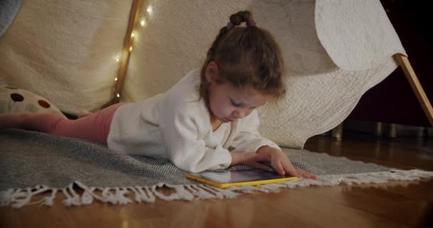 Kleine Mädchen am Abend spielen und sehen Cartoons auf einem Tablet, in einem Zelt. Urteil 1 — Stockvideo
