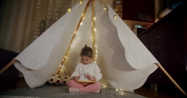 La bambina su gioco di sera e guardare cartoni animati su una targa, in una tenda. Colpo largo — Video Stock