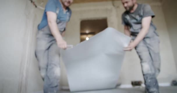 Due operai installano l'isolamento termico sul pavimento. Lavori di riparazione in casa. — Video Stock