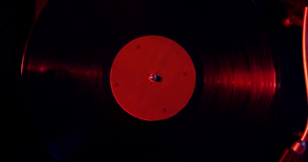 Черный виниловый фон с зеленой наклейкой в центре, вращающийся по кругу в красном свете Версия 2 — стоковое видео
