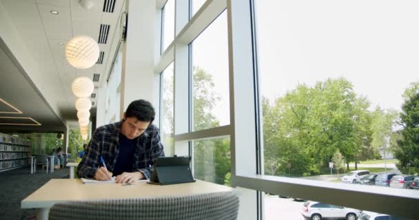 Mahasiswa yang duduk di perpustakaan, menulis dalam sebuah buku catatan, — Stok Video