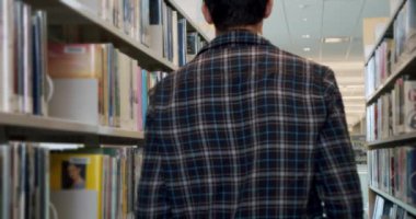 Üniversite öğrencisi kütüphaneye gider ve bir kitap seçmek için durur..