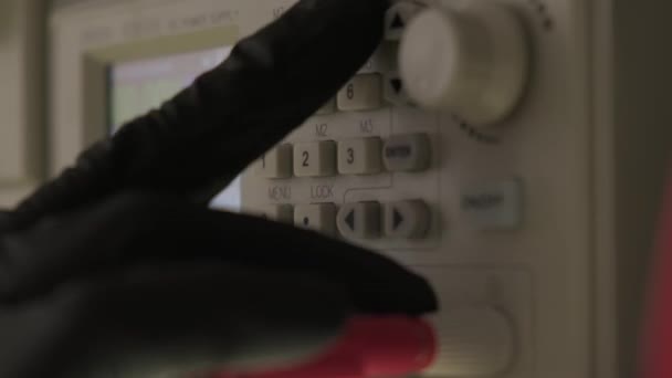 Uma mão de luva preta ajusta o dispositivo em uma oficina de reparo eletrônico no moderno laboratório de eletrônicos, osciloscópio de microprocessador e multímetro. Vista de perto — Vídeo de Stock