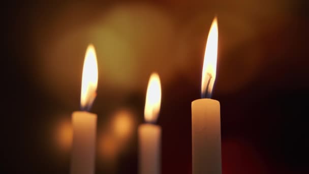 Aus nächster Nähe. Brennende drei Kerzen auf einem Hintergrund aus farbigem, verschwommenem Bokeh. — Stockvideo