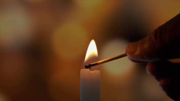 Verfilmung der Verwendung eines Streichholzes, zünden Sie eine Kerze auf einem farbigen verschwommenen Bokeh an — Stockvideo
