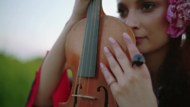 Porträt einer Frau mit einer Blume im Haar, sie hält eine Geige. Nahaufnahme — Stockvideo