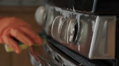 Sarı eldivenli eller mutfakta temizlenir, gaz fayansları yıkanır. Yakın çekim.