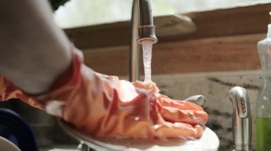 Turuncu eldivenli eller mutfakta bulaşıkları yıkar. Kapat.