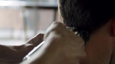 Berberin yakın çekimi genç adamın saçını saç makasıyla kesiyor. Yavaş çekim sürümü 2