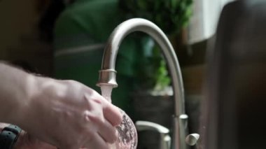 Close up view of Hands in orange gloves wash dishes in the kitchen. 