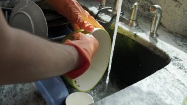Close up view of Hands in orange gloves wash dishes in the kitchen. Slow motion