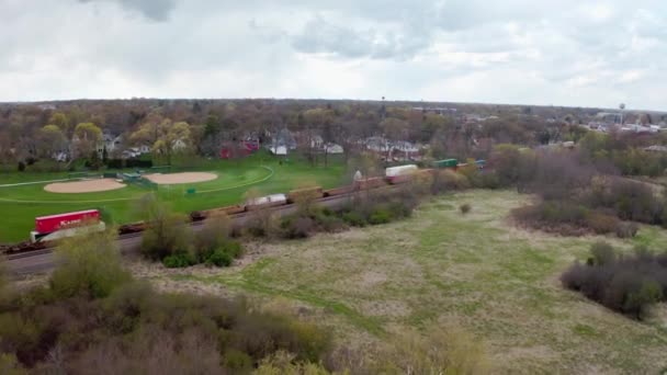 Aerial drone shot of Locomotive with freight railway wagon rides on railroad. Transportation and delivery of cargo in containers between cities. Aerial drone view over train riding through forest — Stock Video