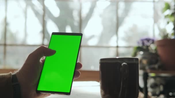 A male hand holds a phone with a mockup green screen, and drinks coffee. Close up shot — Stok video