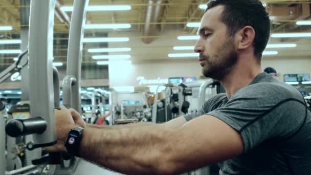 Modern gym, a man sitting down on the training apparatus and training. Slow motion view — Stock Video