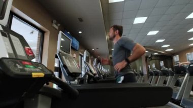 Koşu pistinde yürüyen bir adam, koşu bandında ısınıyor. Yan görünüm ve Yavaş çekim