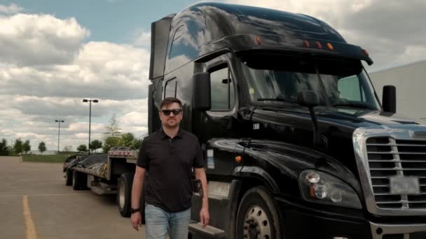 Portret profesjonalnego kierowcy ciężarówki zbliża się do jego ciężarówki i krzyżuje ramiona za nim zaparkowany długi holownik Semi-Truck z przyczepą Cargo — Wideo stockowe