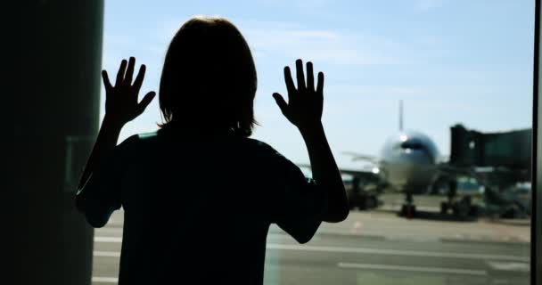 Silueta de un niño cerca de una gran ventana en el aeropuerto, mira a los aviones. Movimiento lento. — Vídeo de stock