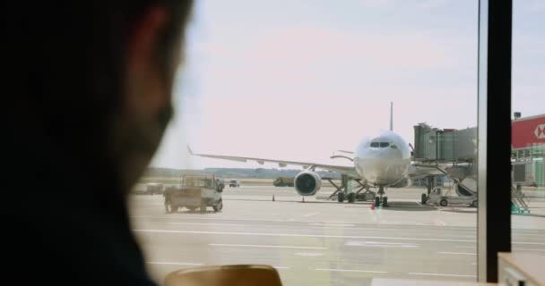 Silhouette di un ragazzo vicino a una grande finestra all'aeroporto, guarda gli aerei e scatta foto su smartphone. Rallentatore. — Video Stock