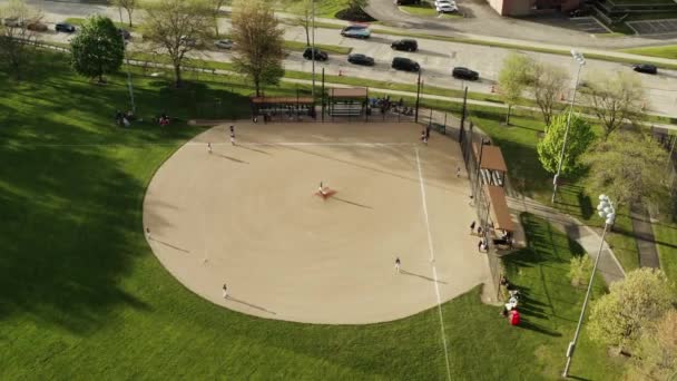 एरियल ड्रोन शॉट। कई बच्चों का दृश्य धूप के दिन पार्क में बेसबॉल फील्ड खेलते हैं। अमरीका — स्टॉक वीडियो
