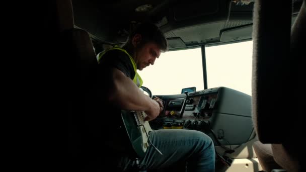 O motorista do caminhão está sentado na cabine e tocando guitarra. Futuro largo — Vídeo de Stock