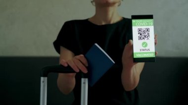 Kadın, çantasında seyahat izni olan akıllı telefon ve aşı pasaportu gösteriyor. Görüntüyü kapat