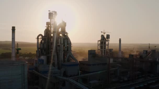 Vue rapprochée du drone aérien d'une cimenterie à silhouette avec structure industrielle élevée dans la zone de production industrielle au coucher du soleil. — Video