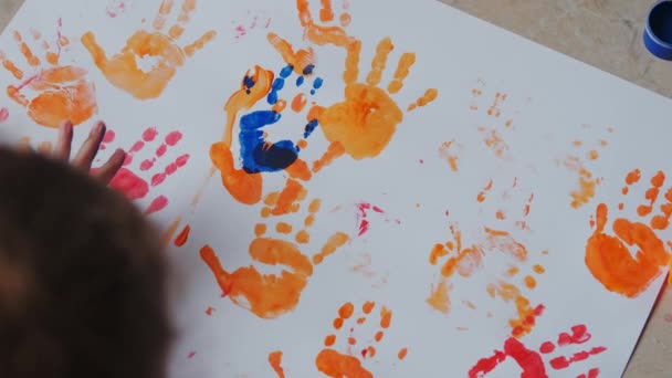 Menina com tintas nas mãos desenha em papel branco. Vista superior — Vídeo de Stock