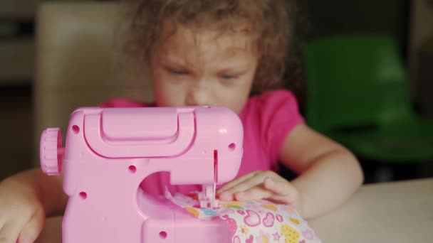 Το κοριτσάκι ράβει ρούχα για κούκλες σε ένα μηχάνημα παιχνιδιών. Κλείσε. — Αρχείο Βίντεο