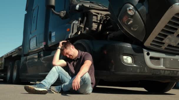 A truck driver sits on the ground near a broken truck — Stock Video