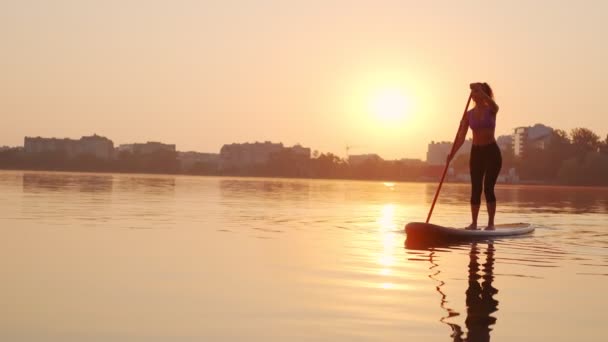 Захід сонця, жіночий силует на озері встав на весло дошки суп, повільний рух — стокове відео