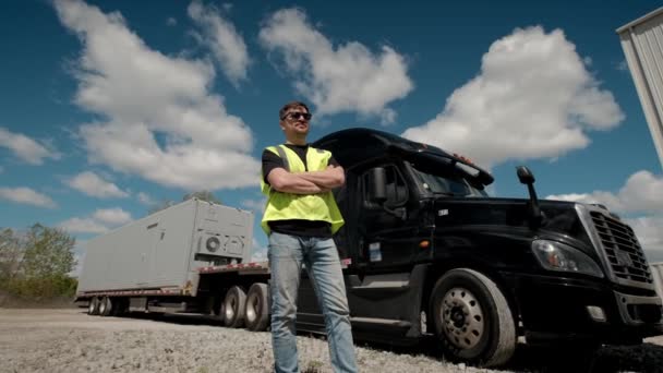 Professionele Truck Driver in een gele vest nadert zijn truck en kruist zijn armen achter hem geparkeerde Long Haul Semi-Truck met Cargo Trailer. Breed schot — Stockvideo