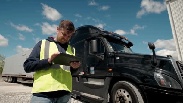 Vrachtwagenchauffeur die bij de truck staat in een geel vest en een tablet gebruikt om een lookbook te vullen — Stockvideo