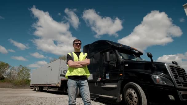 Motorista de caminhão profissional em um colete amarelo se aproxima de seu caminhão e cruza os braços Atrás dele estacionado Long Haul Semi-Truck com reboque de carga — Vídeo de Stock