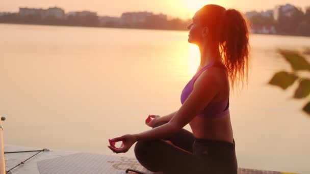 Jonge vrouw die yoga doet op SUP board bij zonsondergang. Langzame beweging — Stockvideo