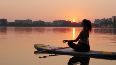 Gün batımında SUP panosunda yoga yapan genç bir kadın. Yavaş çekim