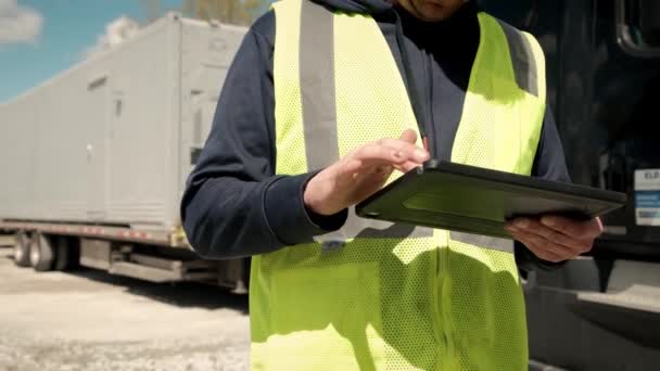 Tutup pandangan pengemudi truk yang berdiri di samping truk dengan rompi kuning dan menggunakan tablet untuk mengisi buku lihat — Stok Video