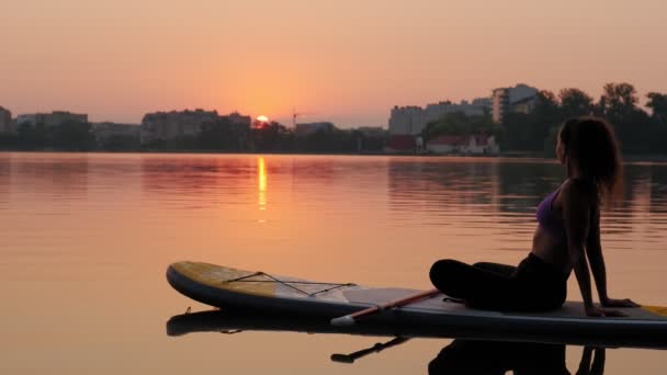 Young woman on SUP board He sits in a relaxed position and looks at the sunrise — Vídeo de Stock